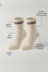 Two beige BODYBORN crew-length socks with brown double stripes, displayed upright and labeled with product features including moisture-wicking material, arch support, antimicrobial and antifungal half-terry construction, all-over cushioning through the foot and leg, and seamless toe