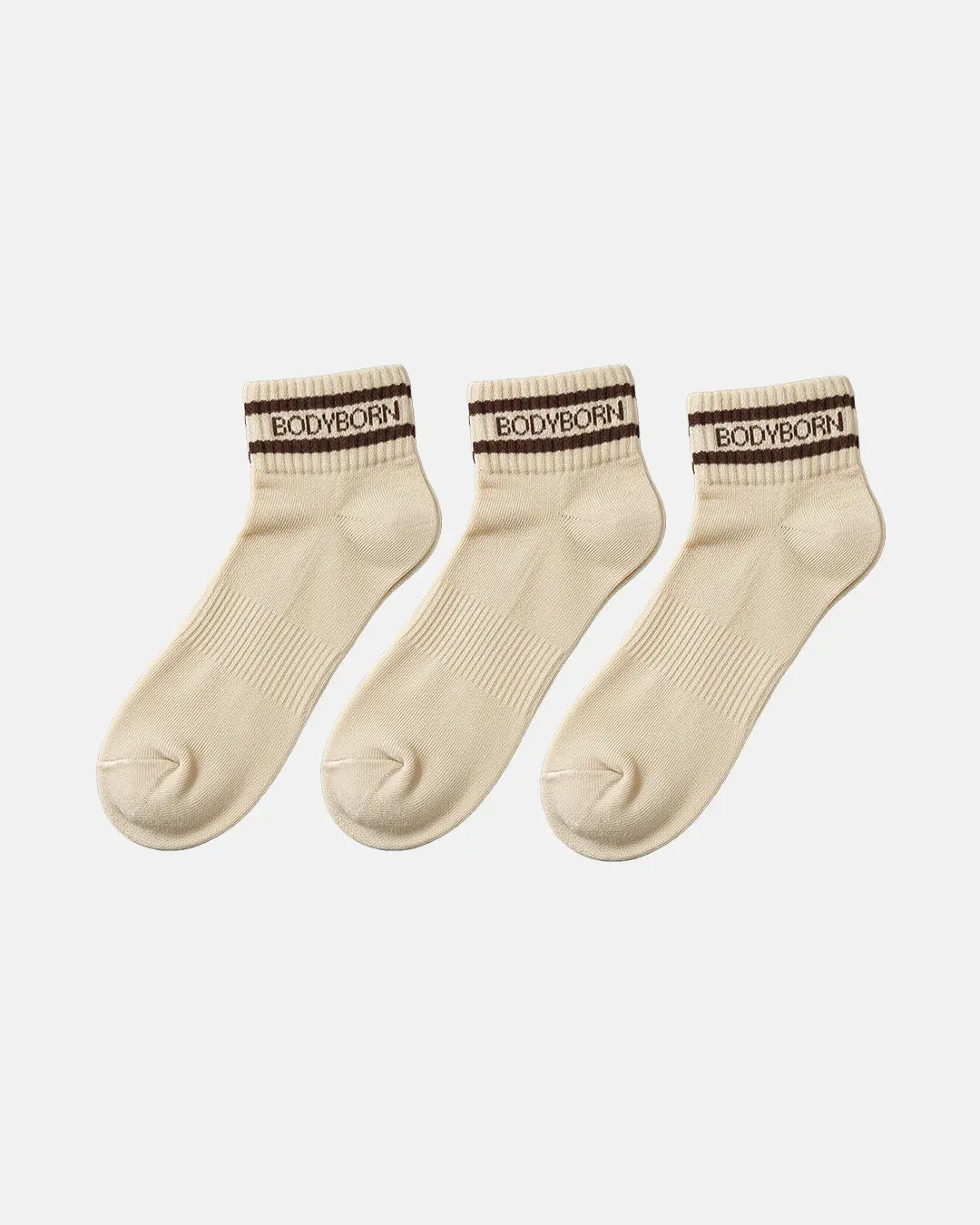 Three beige ankle socks arranged side by side on a white background, each designed with ribbed fabric and a brown BODYBORN branded stripe around the cuff