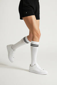 Person wearing black shorts, white socks with black stripes, and white sneakers on a light gray background in crew size soft and comfortable