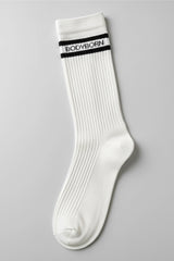 White socks with black stripes and 'BODYBORN' branding worn by a woman sitting on a stool in crew size