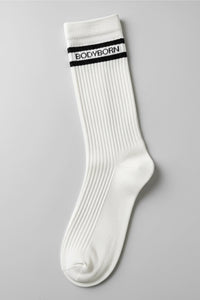 White socks with black stripes and 'BODYBORN' branding worn by a woman sitting on a stool in crew size
