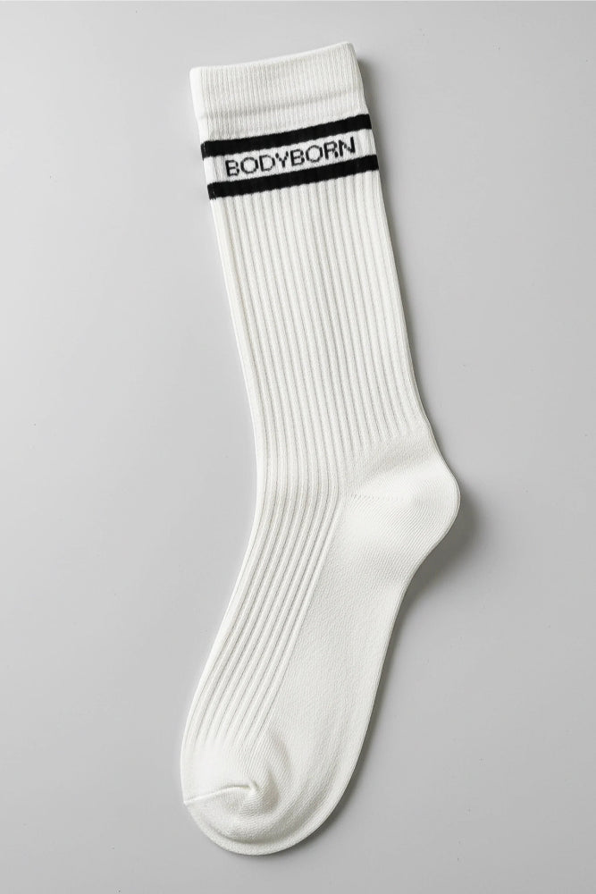 White socks with black stripes and 'BODYBORN' branding worn by a woman sitting on a stool in crew size