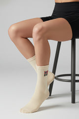 Person wearing beige socks with a logo, sitting on a stool against a plain background in crew size premium soft and comfortable