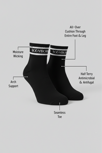Two black BODYBORN ankle-length socks displayed upright with white logo stripe, labeled with moisture-wicking material, arch support, antimicrobial and antifungal half-terry construction, all-over cushioning through the foot and leg, and seamless toe