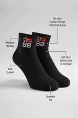 Two black BODYBORN crew-length socks displayed upright with embroidered BB logo and red-white flag, labeled with features including moisture-wicking material, arch support, half-terry antimicrobial and antifungal construction, all-over cushioning through the foot and leg, and seamless toe