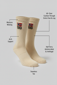 Two beige BODYBORN crew-length socks displayed upright with embroidered BB logo and red-white flag, labeled with moisture-wicking material, arch support, all-over cushioning through the foot and leg, antimicrobial and antifungal half-terry construction, and seamless toe