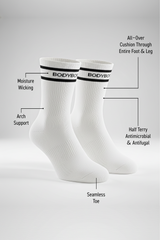 Two white BODYBORN ankle-length socks with black stripe and logo displayed upright, featuring labeled benefits such as moisture-wicking material, arch support, all-over cushioning through the foot and leg, antimicrobial half-terry knit, and seamless toe